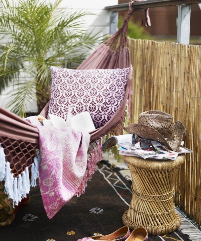 brise vue de balcon de canisse en bambou, table basse tressée et hamac couleur mauve, palmier sur deco terrasse avec tapis marron oriental