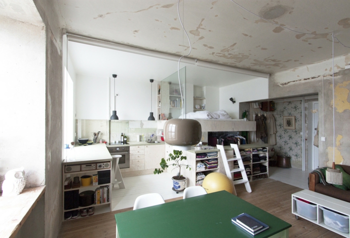 appartement loft industriel, petite cuisine moderne, sol en bois, plafond en béton, lit avec étagères