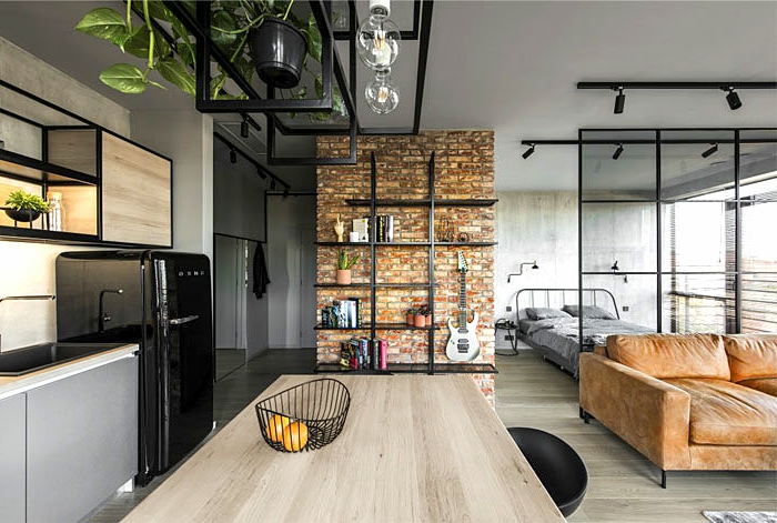 appartement loft, grande table rectangulaire, sofa marron, frigo noir, étagère avec placards, étagère industrielle, plantes suspendues en pots