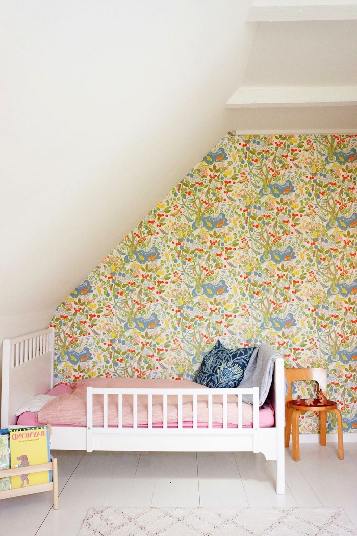 une chambre d'enfant vintage aménagée sous les combles avec petit lit blanc posé en sous-pente contre le mur d'accent en papier peint vintage floral