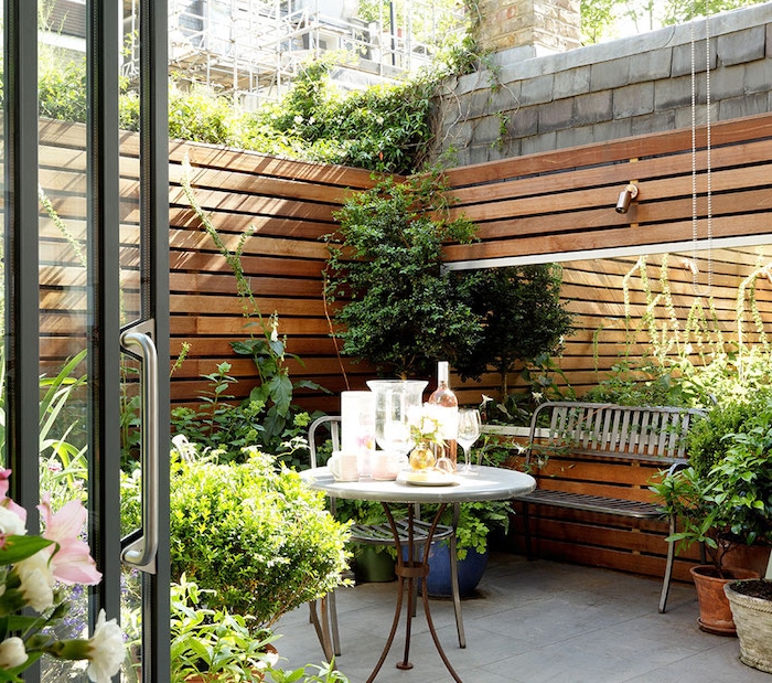 idee deco terrasse avec revetement en dalles de pierre, table ronde original, banc en metal, plantes vertes deco exterieur