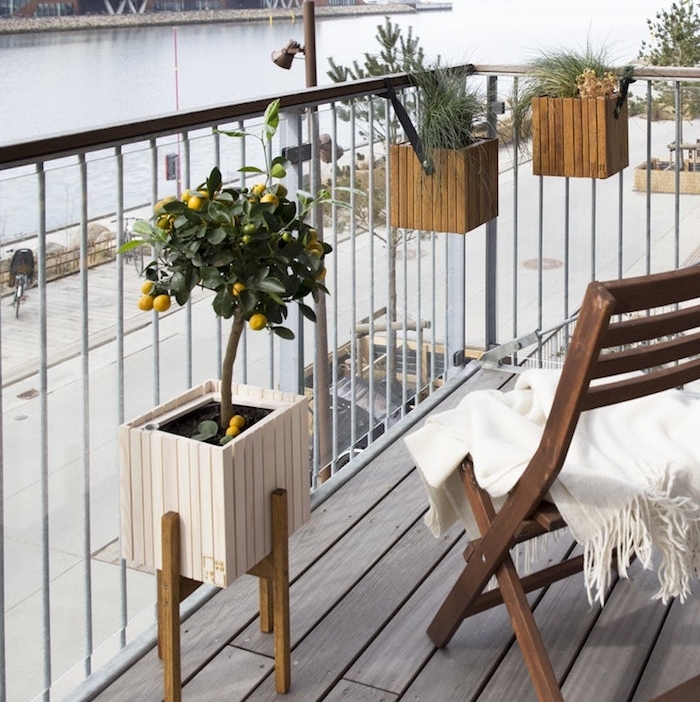 bacs à fleur accrochés sur un garde corps de balcon et pot à citronnier, chaise bois pliante sur balcon en bois