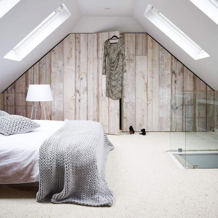 une chambre à coucher au design épuré aménagée sous les combles avec un dressing sous pente à portes imitation bois
