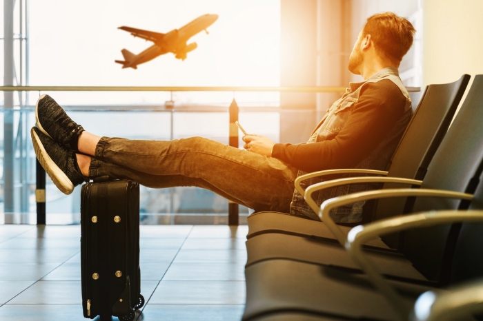 un homme assis confortablement dans la salle d'attente de l'aéroport regardant un avion qui décolle, astuces pour mieux organiser son voyage en avion