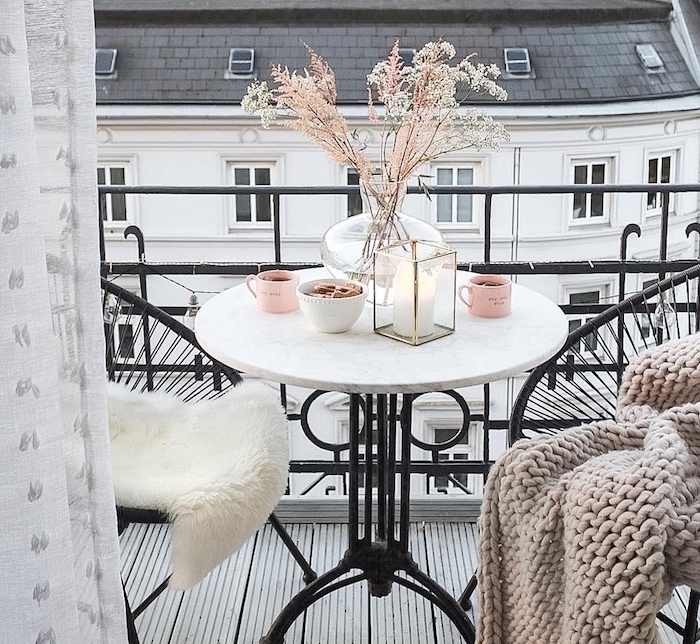 petit dejeuner sur un balcon cocooning avec table ronde elegante et deux chaises en fer noires sur sol en revetement bois