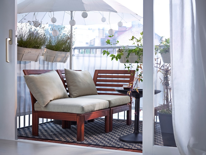 brise vue balcon en toile blanche, parasol blanc pour ombrage, canapé en bois, table basse ronde et tapis noir et gris, bas à fleurs suspendus