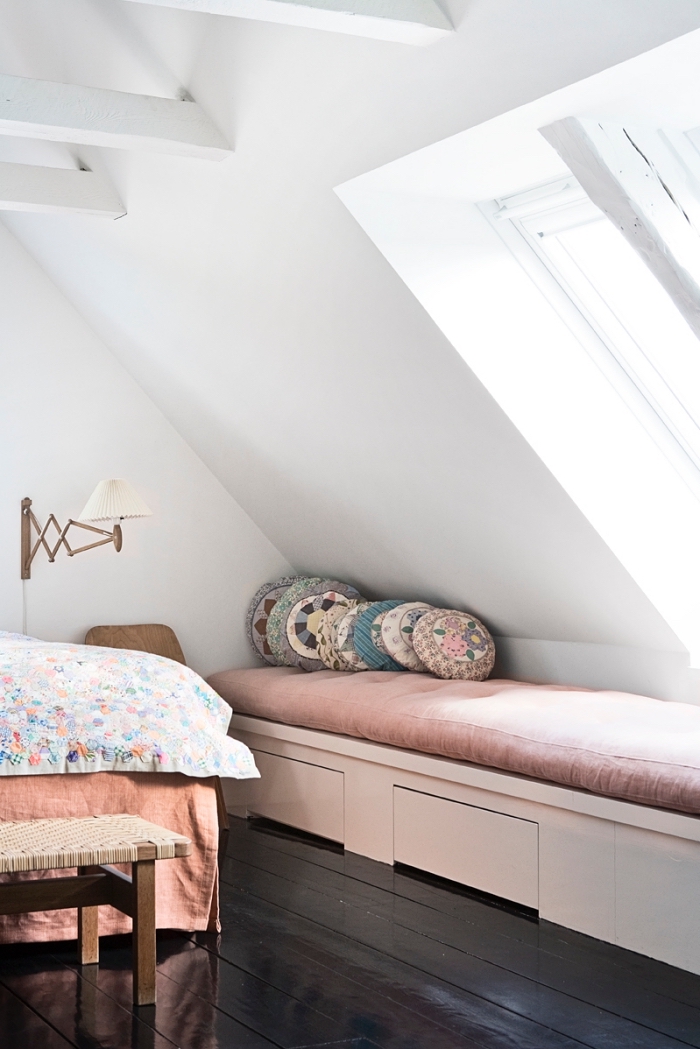 une chambre à coucher mansardée avec plancher en bois foncé et banquette sous fenêtre aménagée sous pente