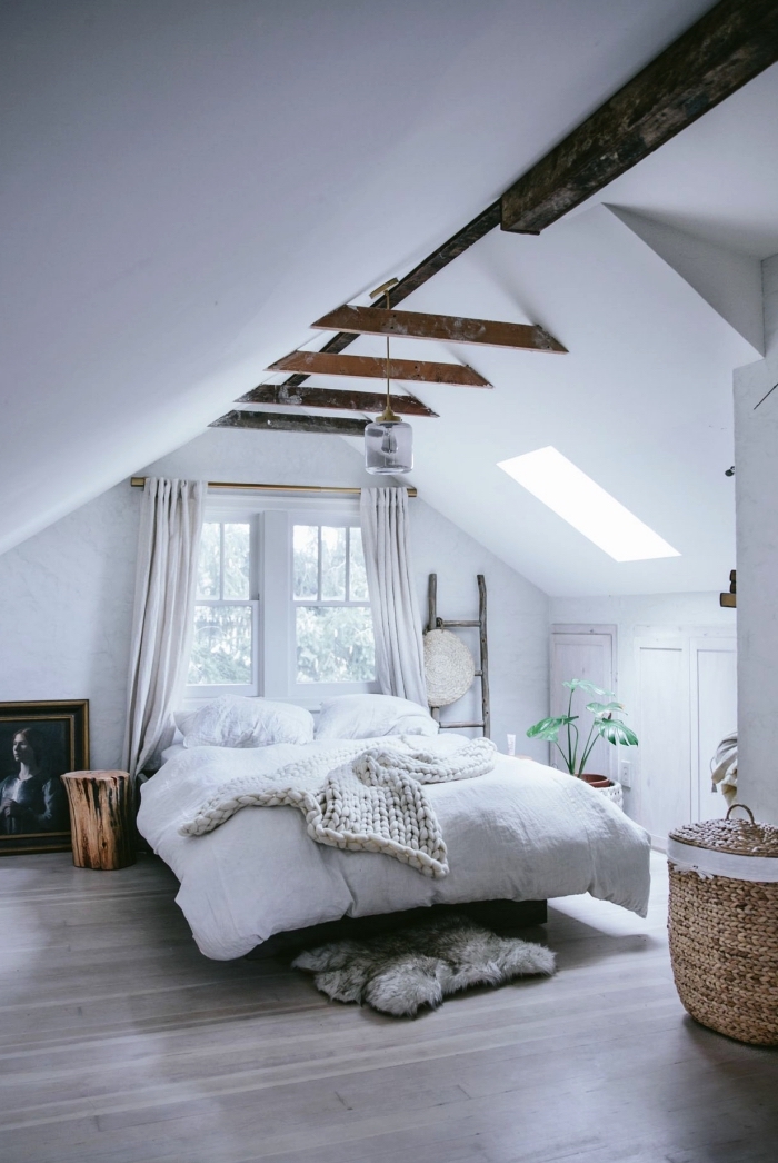 une chambre à coucher vintage scandinave aux accents rustiques grâce aux poutres apparentes, avec placard sous pente qui se fond dans le décor blanc