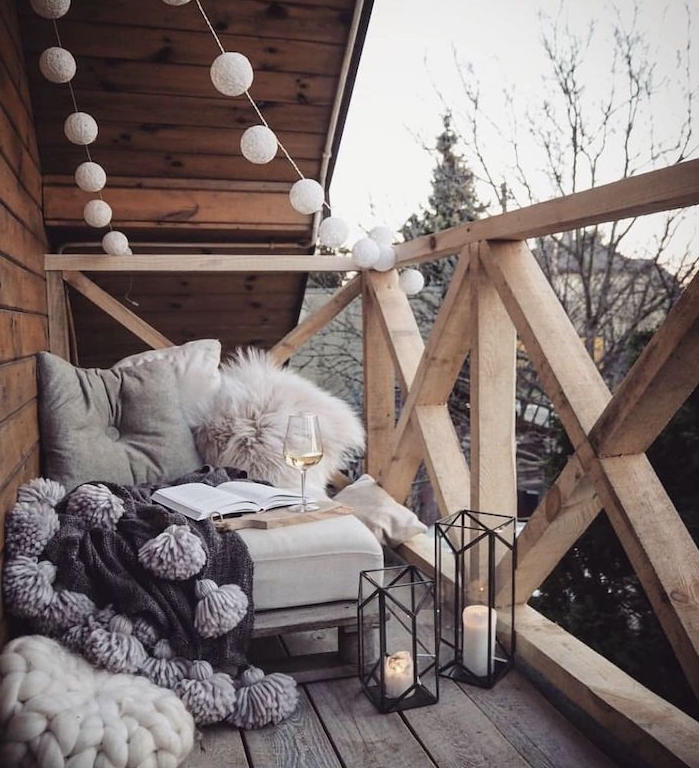 guirlande boule exterieur, fauteuil cocooning avec coussins et plaid, lanternes à bougies, terrasse en bois d une maison en bois, deco scandinave sur balcon