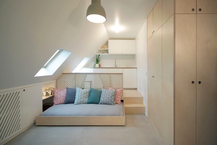 design minimaliste de studio avec cuisine sous comble en blanc, lit cocooning en bois avec coussins colorés et armoire bois, aménagement de studio