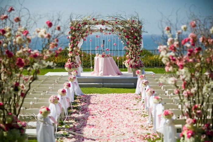 mariage en blanc et rose, cérémonie à l'extérieur, pétales de roses parsemées au sol, banquettes blanches
