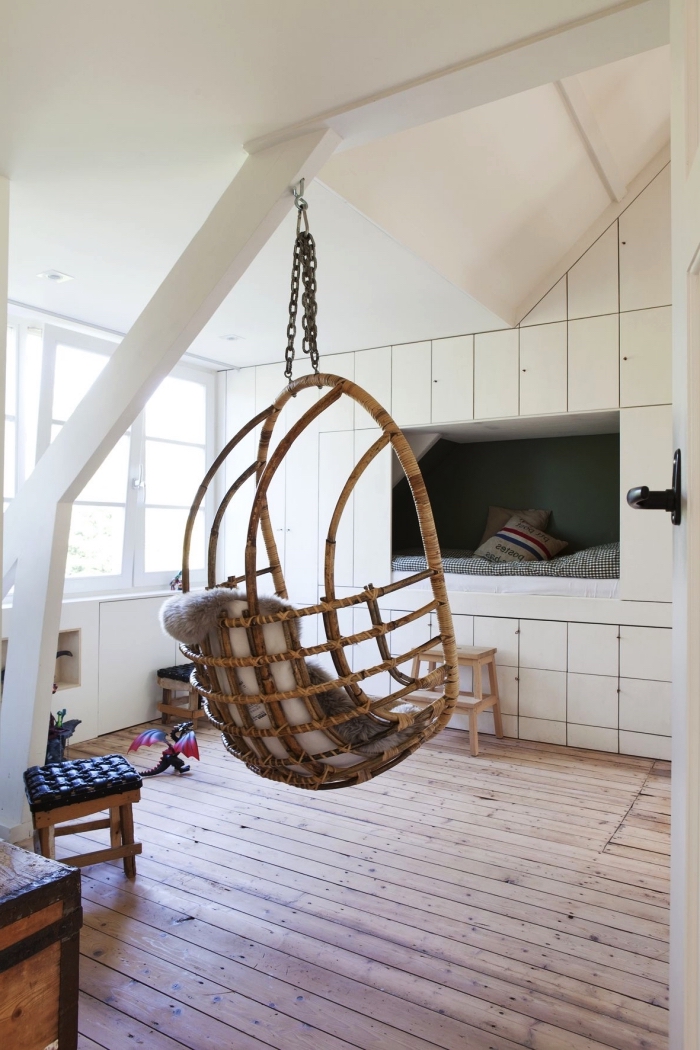 une chambre d'enfant scandinave avec fauteuil suspendu, meuble sous pente encastré au mur avec niche murale façon lit cabane