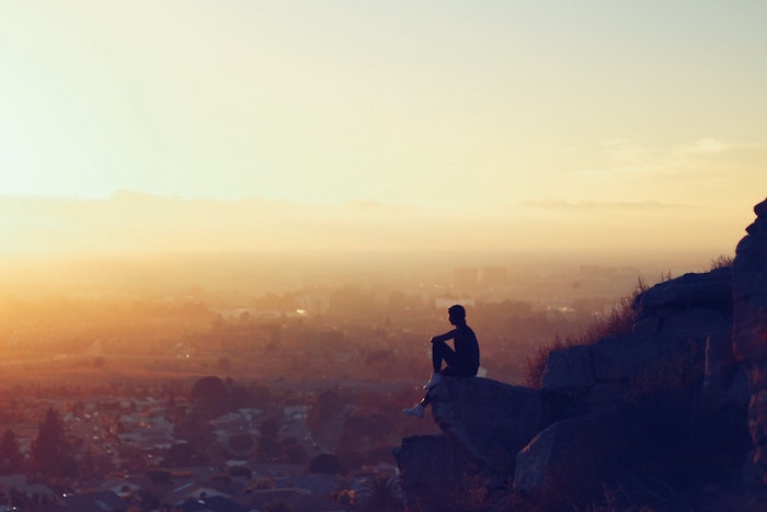 Homme assise sur un rocher avec belle vue au coucher de soleil, beau paysage urbain, image à utiliser pour fond d'écran libre de droit