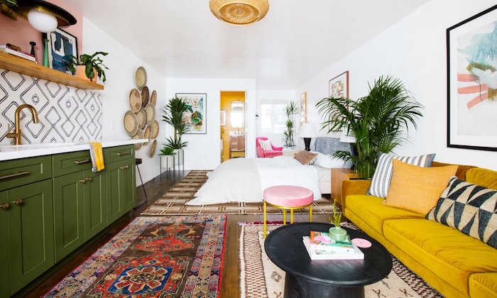 canapé jaune moutarde en face d une cuisine vert olive avec étagère bois ouverte, tapis oriental, lit cocooning, deco murale artistique, aménager un studio boheme chic exotique