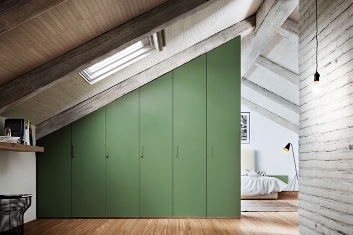 une armoire sous pente verte qui sépare l'espace de la chambre à coucher mansardée en deux