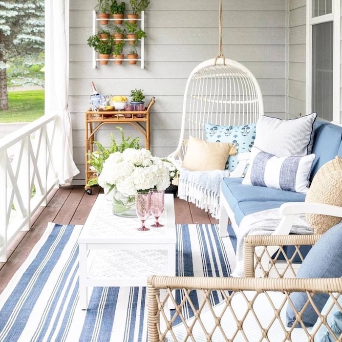fauteuil suspendu balancelle, canapé blanc décoré de coussins bleu et blanc, table basse blanche, tapis à rayures bleu et blanc, mur végétal extérieur sur un balcon cosy