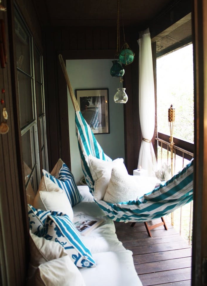 hamac d exterieur et canapé d exterieur sur un balcon habillé de bois avec plusieurs coussins décoratifs cocooning, rideau de balcon blanc
