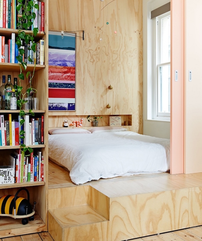 lit en simple matelas sur estrade de bois avec bibliothèque à coté, niche murale dans mur de bois, portes coulissantes de separation