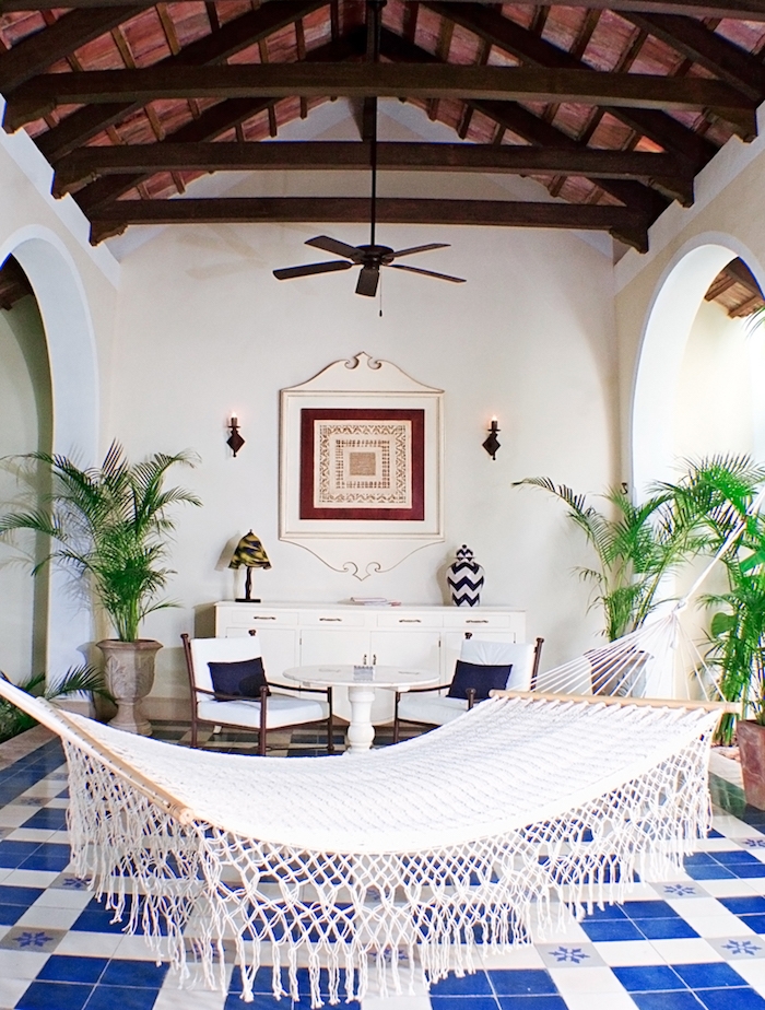 balcon couvert avec toiture en bois, hamac d exterieur, carrelage sol bleu et blanc, meuble blanc, table et chaises pour constituer un coin repos, plantes exotiques en pots