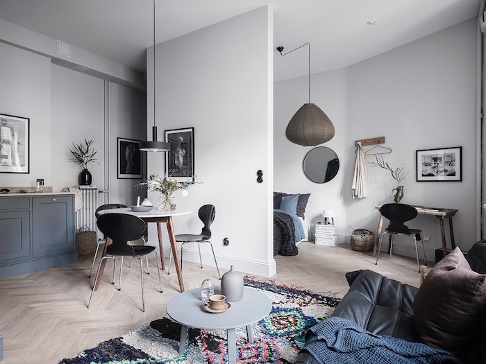 idée comment aménager un studio spacieux avec une chambre à coucher séparée d un mur, coin salon avec canapé cuir noir, table basse ronde, tapis original, table entourée de chaises scandinaves