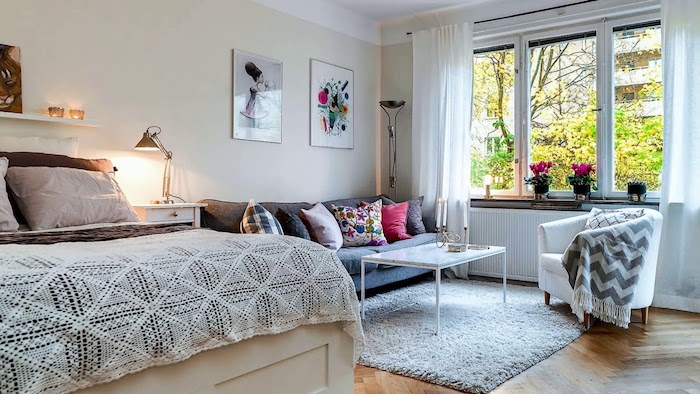 canapé gris et petite table basse blanche design sur tapis gris, fauteuil gris, lit style traditionnel, murs beige clair, cadres décoratifs