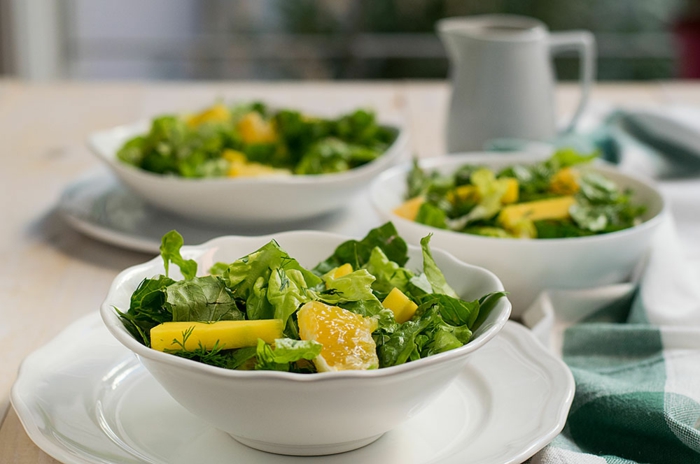 idée salade, laitue, mangue et orange, carafe blanc, trois assiettes remplies de salade verte