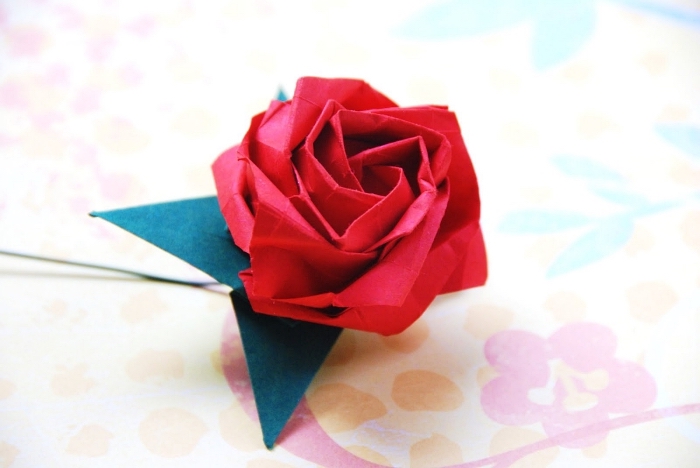 modèle d'origami fleur rose avec ses feuilles vertes en papier, joli pliage de rose délicate en papier