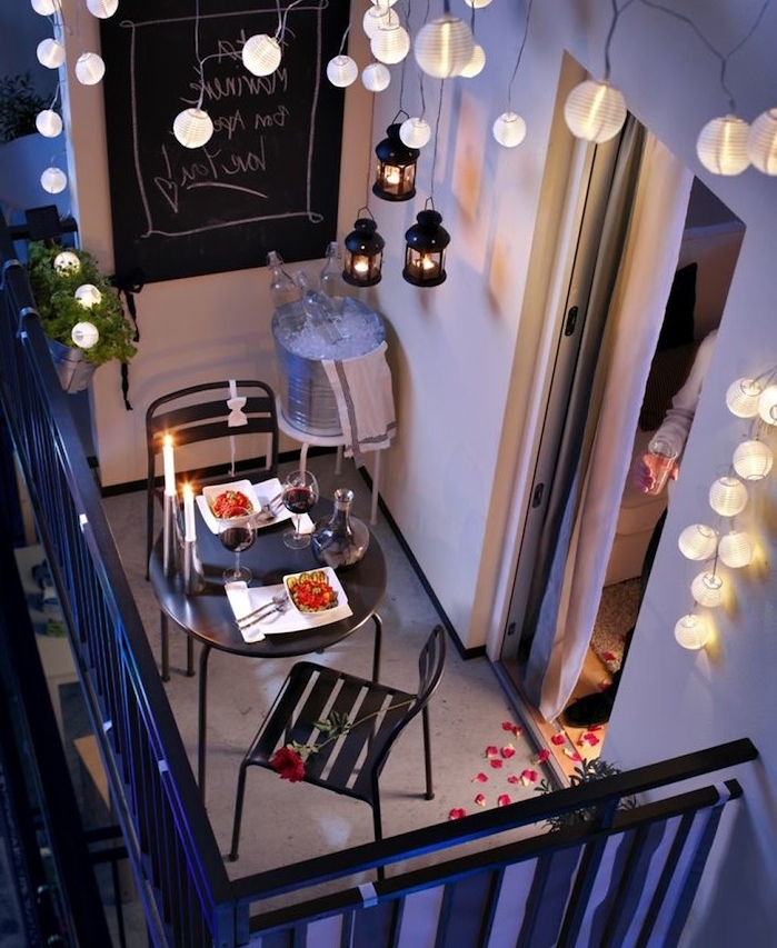 decoration de balcon romantique avec guirlande lumineuse, table et chaises en metal noires, organiser un diner romantique, lanternes suspendues, guirlande boule lumineuse pour ambiance cosy