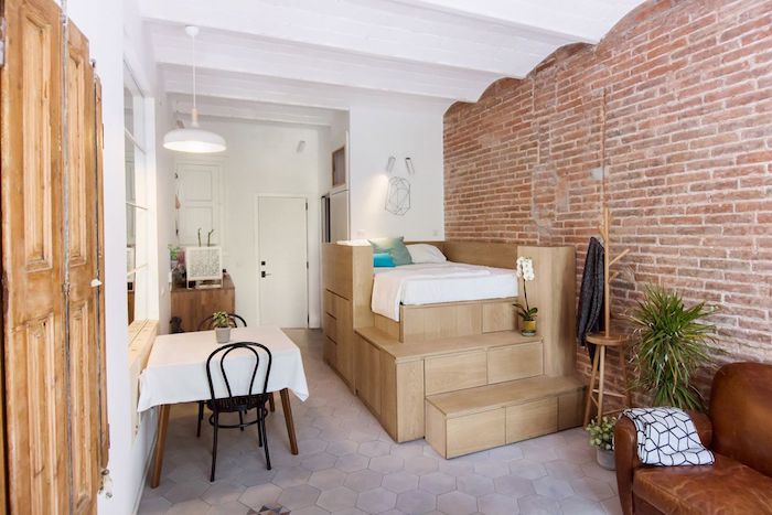 lit sur estrade en bois à coté d un mur de briques, coin repas et canapé en cuir design, aménagement studio 25 m2