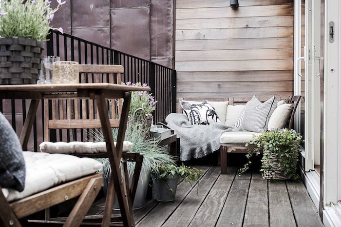balcon en bois avec canapé d angle de bois décoré de coussins gris, chaises et table bois design, plantes en pots, garde corps noir