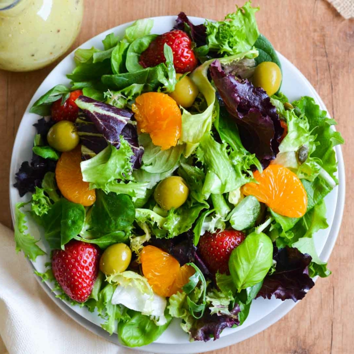 salade aux roquettes et aux olives vertes, assiette blanche, clémentine, fraises, salade composée originale 