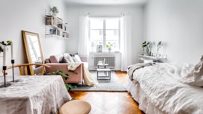 deco nordique dans une chambre à coucher design avec canapé rose, lit blanc, table simple, parquet bois,étagère pour livres