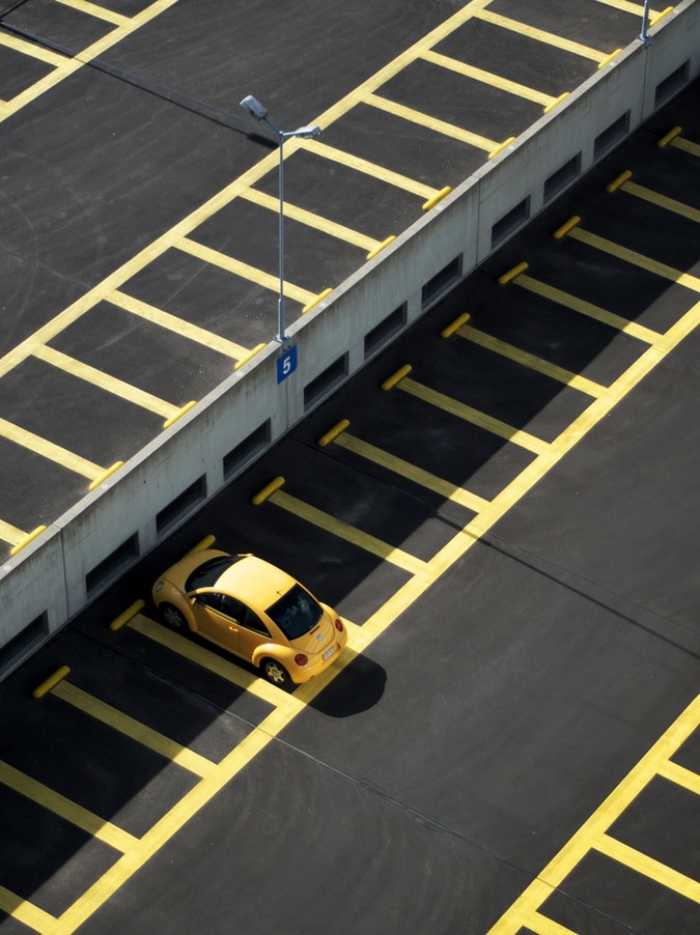 une zone de stationnement avec des places de parking libres délimitées par des lignes jaunes, une voiture jaune garée sur une place de parking