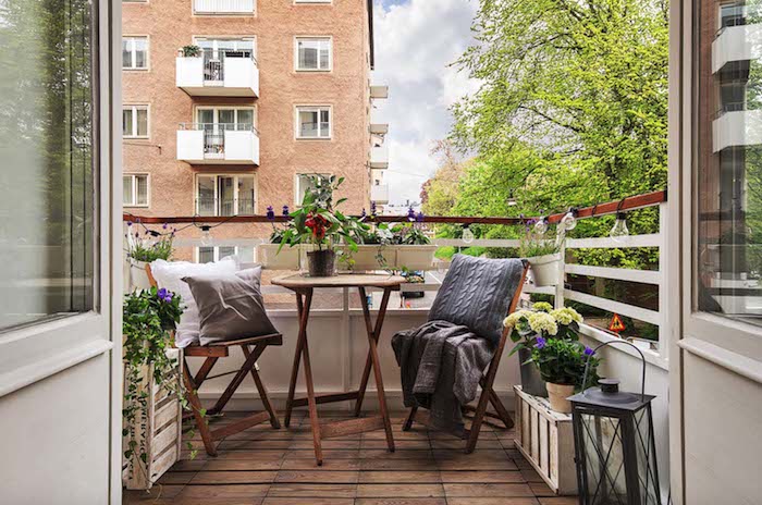 aménagement petit balcon avec vue, table ronde basse et chaises de bois sur balcon avec revetement sol bois, coussins gros et plaid, pots de fleurs fleuries
