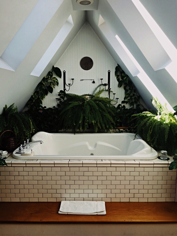 aménagement petite salle de bain sous les combles, baignoire balnéo encastrée sous pente entourée de plantes vertes pour une ambiance zen et nature
