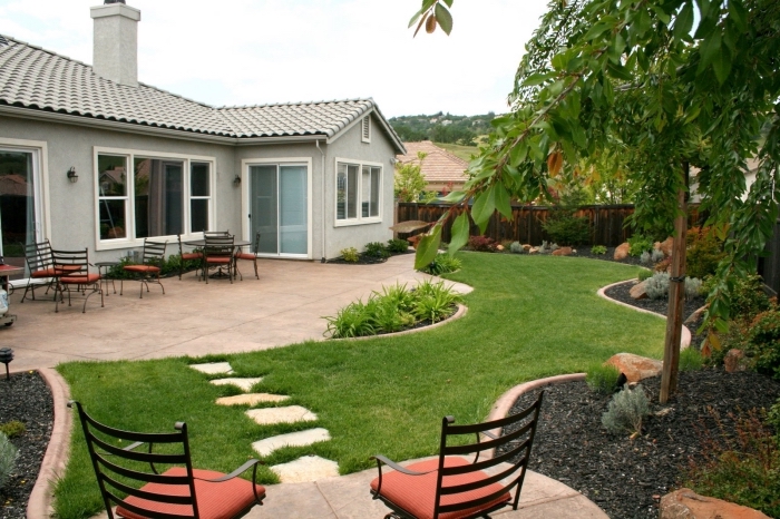 idée comment décorer un espace extérieur, cour arrière avec pelouse et petite terrasse à revêtement dalles aménagée avec meubles fer