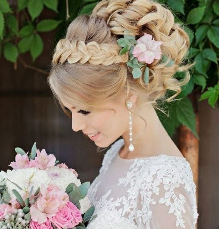 coiffure mariage chignon bouclé avec tresse sur le front et volume sur le dessus, accessoire pour cheveux fleur rose, robe de mariée dentelle