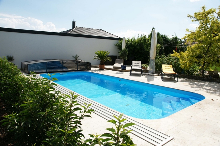 une piscine coque rectangulaire avec plage en travertin beige clair aménagée dans l'arrière-cour et entourée de verdure