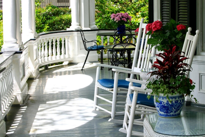 terrasse blanche, chaises balançantes blanches, pot de fleur style marin, plantes fleuries, table en fer forgé