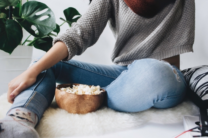 comment bien se reposer à la maison, photo ambiance cozy dans un salon blanc et jeune fille avec bol de popcorn, fond d écran cool