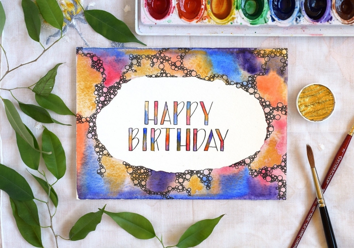 faire une carte d'anniversaire colorée avec une bordure décorée à l'aquarelle, lettrage manuscrit joyeux anniversaire multicolore