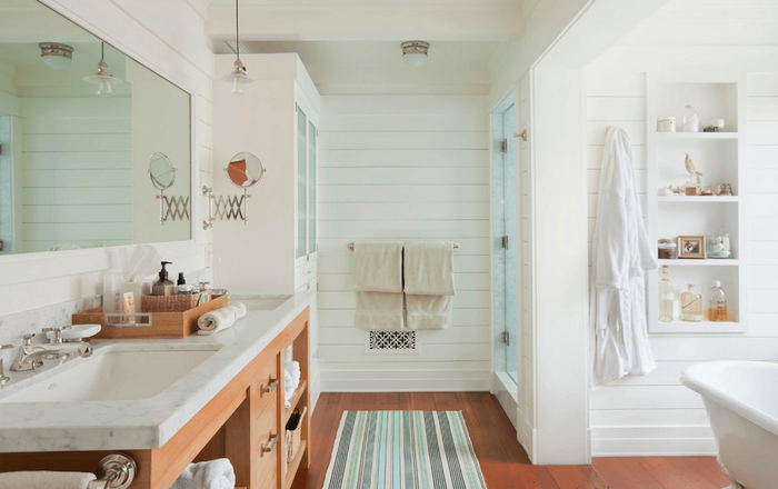 Grand placard, rangement étagère blanche dans le mur, baignoire et douche séparés, tapis de salle de bains bleu, vert et gris et meuble lavabo bois avec nuance rose 