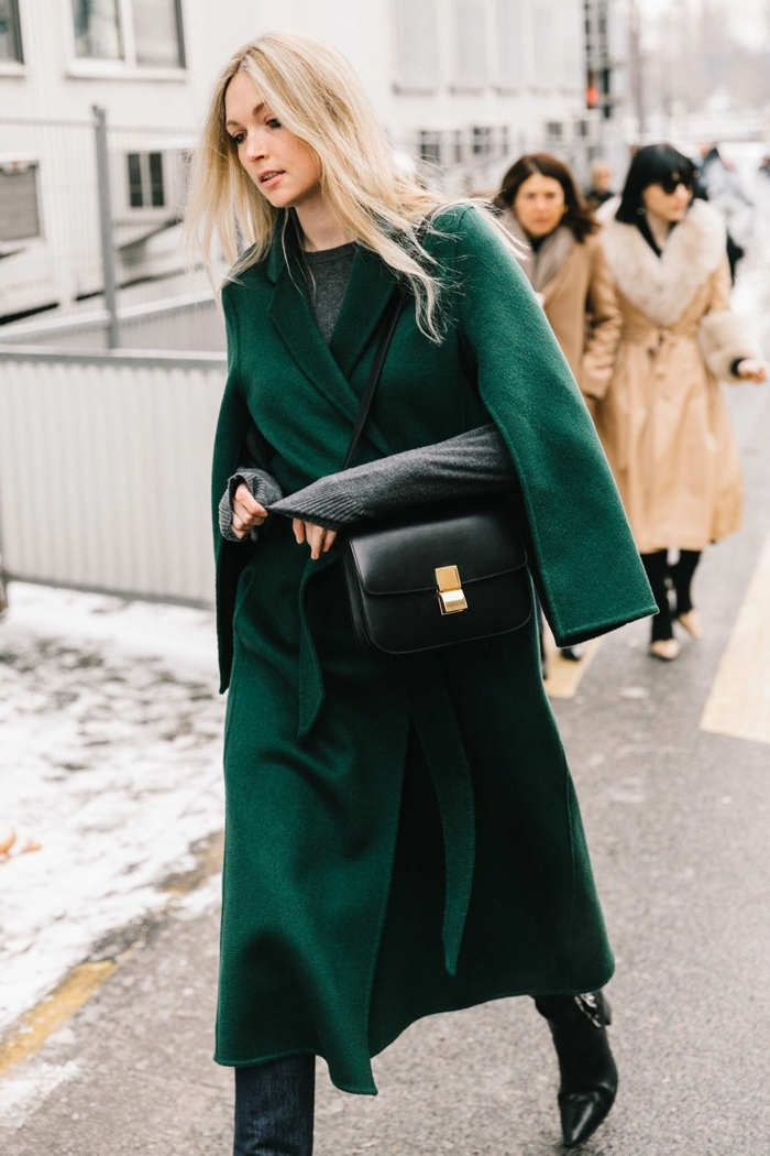 long manteau vert émeraude, sac noir, fermoir doré, cheveux blonds, bottes noires