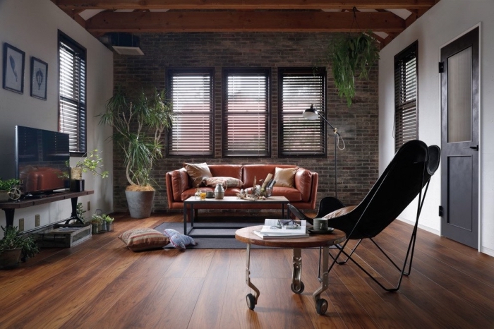 modèle de canapé style industriel en cuir marron, revêtement mural en briques, plantes vertes d'intérieur style bohème