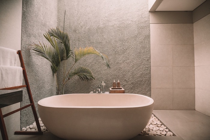 Palmier dans pot sur sol pierres zen, échelle rangement basse, salle de bain en bois et blanc, belle salle de bain moderne