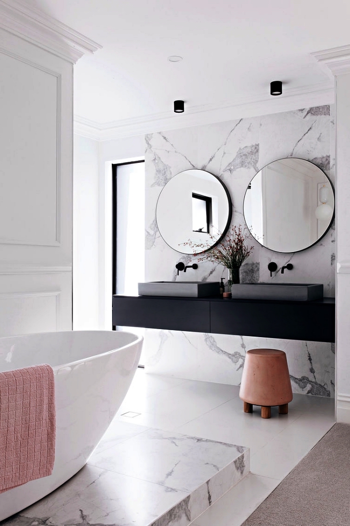 salle de bain de luxe avec crédence en marbre qui s'accorde avec le podium de la baignoire îlot, salle de bain au design épuré avec meuble sous vasque flottant en noir mat
