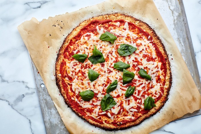 idee de pizza avec croute sans gluten, pâte à pizza avec chou fleur, mozzarella, nappée de sauce tomate, basilic et encore de fromage