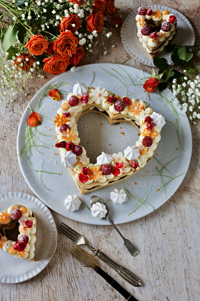gateau coeur sur une base biscuit au décor de meringues, fruits rouges et fleurs comestibles