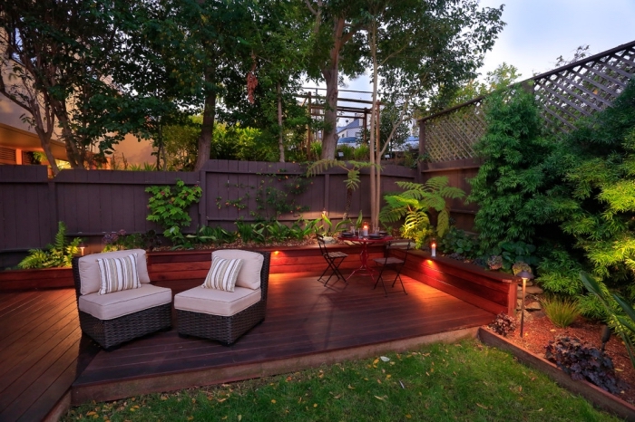 aménager son jardin avec meubles tressés, décoration palissade en bois foncé avec plantes grimpantes et éclairage