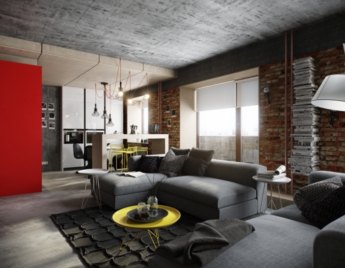 aménagement studio aux murs briques et plafond béton avec pan de mur rouge, modèle de petit canapé d'angle gris